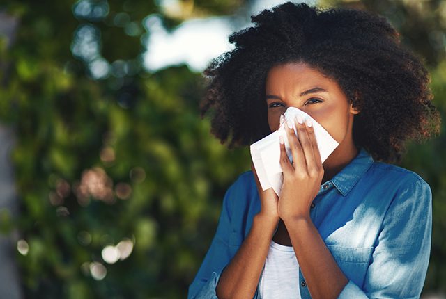 Portrait of a young woman blowing her nose with a tissue outside