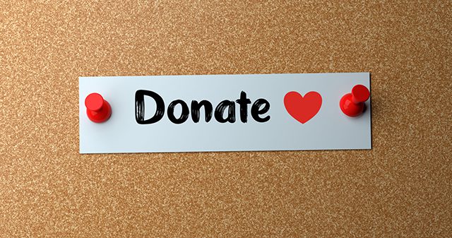 A piece of paper with the word "Donate" and a heart written on it pinned to a cork board