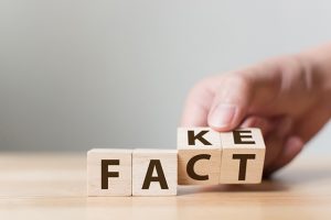 A person changing wooden block letters from spelling "Fake" to spelling "Fact"